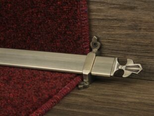 Louis design of stair rod with fleur-de-lys end, antique brass on red carpet