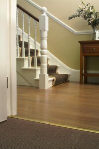 Posh carpet trim, brass, fitted carpet to wood with hall and staircase behind