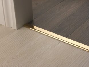 Premier Vinyl Edge floor edging, self-adhesive, shown between vinyl & timber, Polished Brass