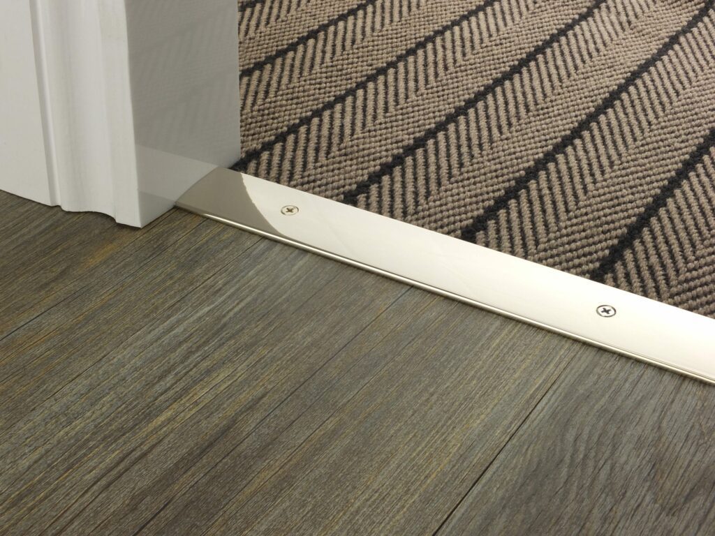 Premier Cover plate 38mm polished nickel with matching screws shown connecting a brown floorcovering to wooden floor