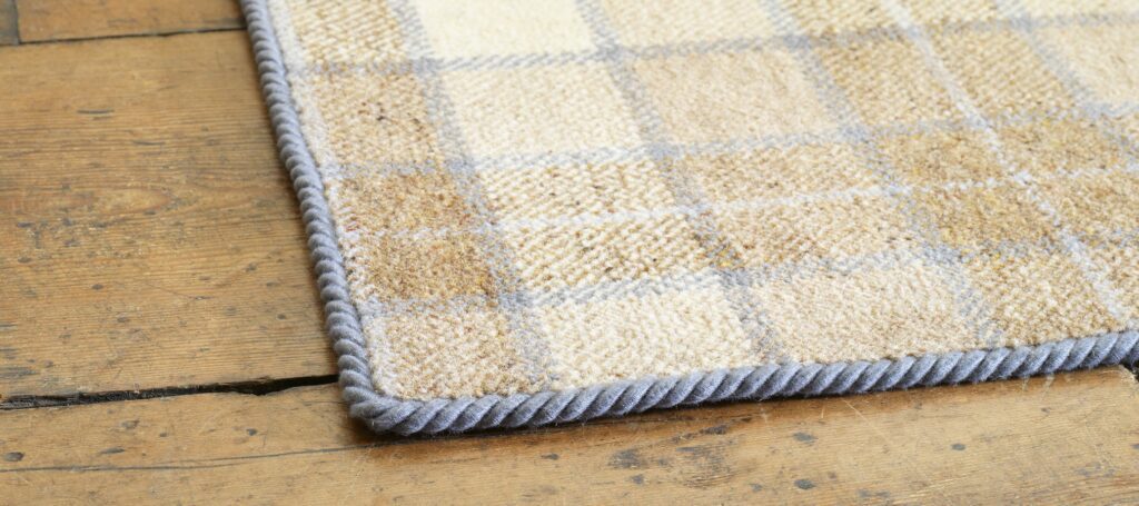 Dusky blue rug binding tape applied to a tartan rug on a wooden floor