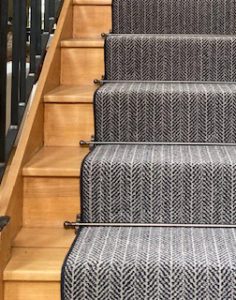 Balladeer stair rod design in antique bronze on grey striped runner stair carpet with wrought iron bannister